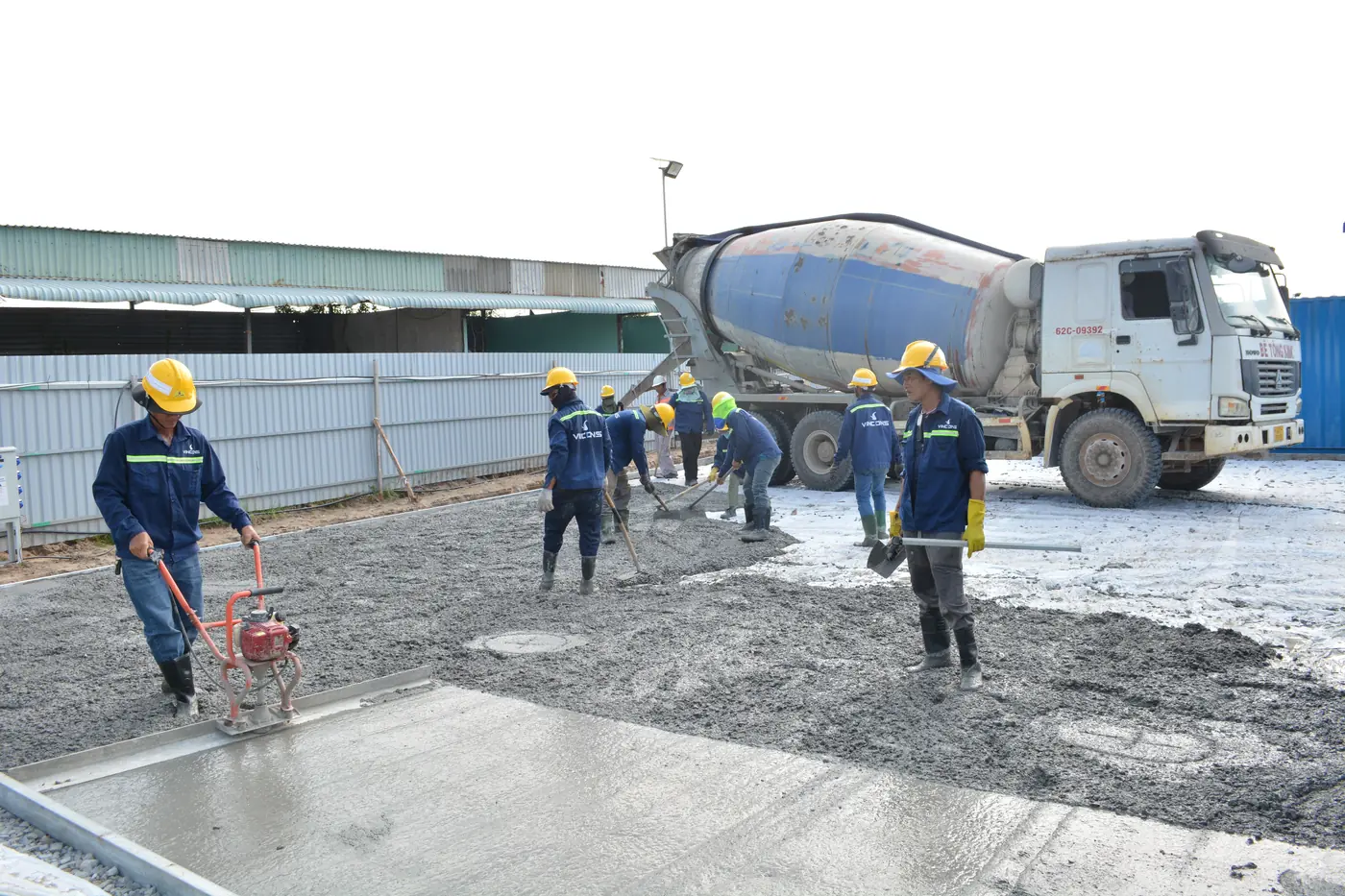 A concrete crew placing and power-screeding a slab as the mixer truck discharges
