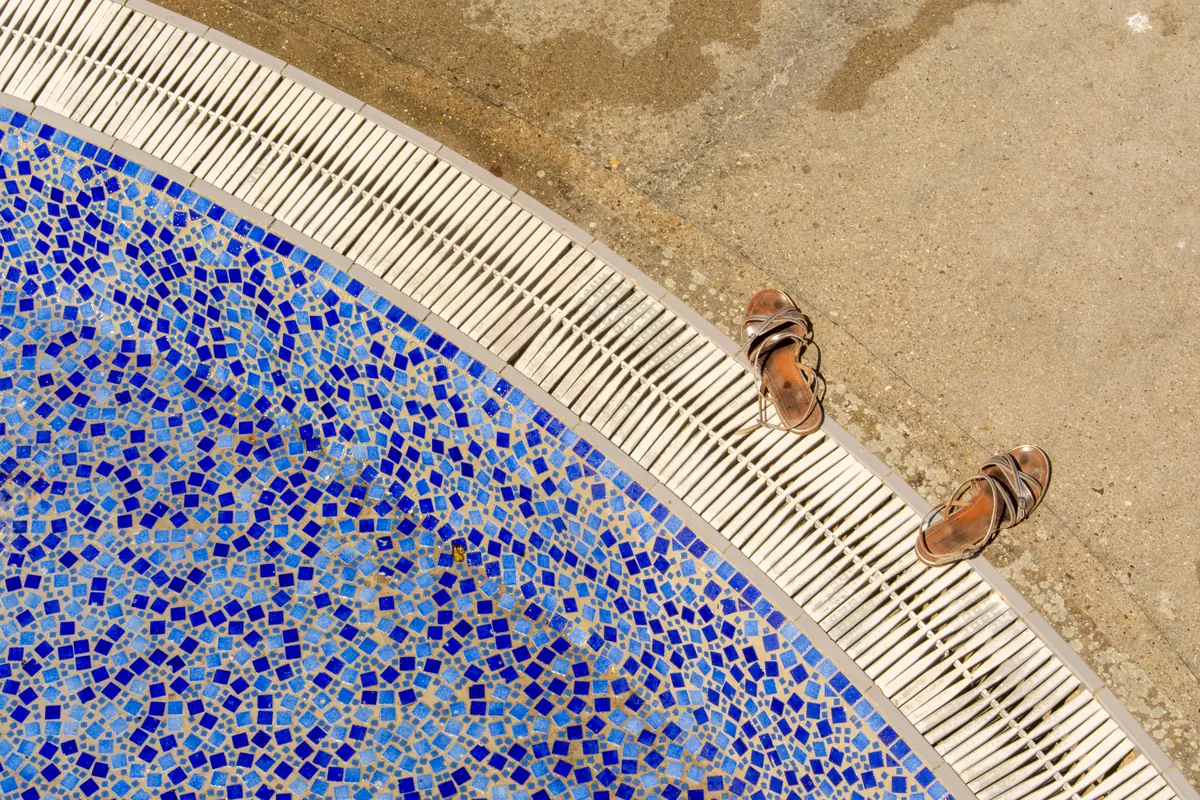 A concrete pool deck meeting a mosaic-tiled pool edge and drainage channel
