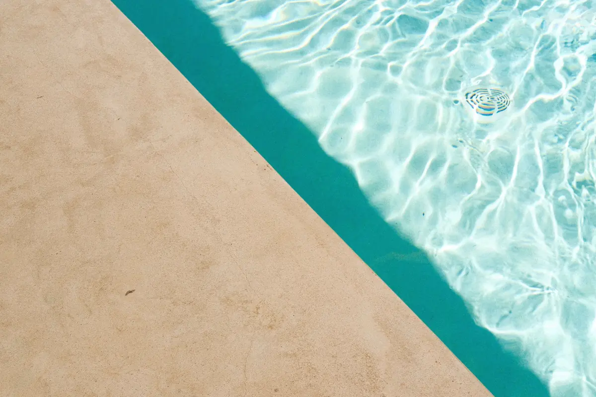 A plain broom-finished concrete deck running to the waterline of a swimming pool
